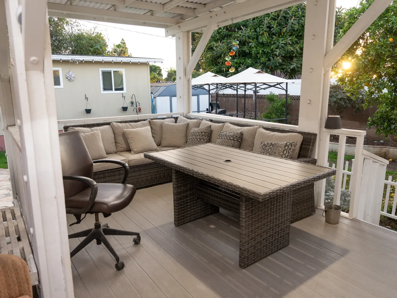 Covered outdoor patio area with comfortable seating and table under white pergola overlooking residential backyard