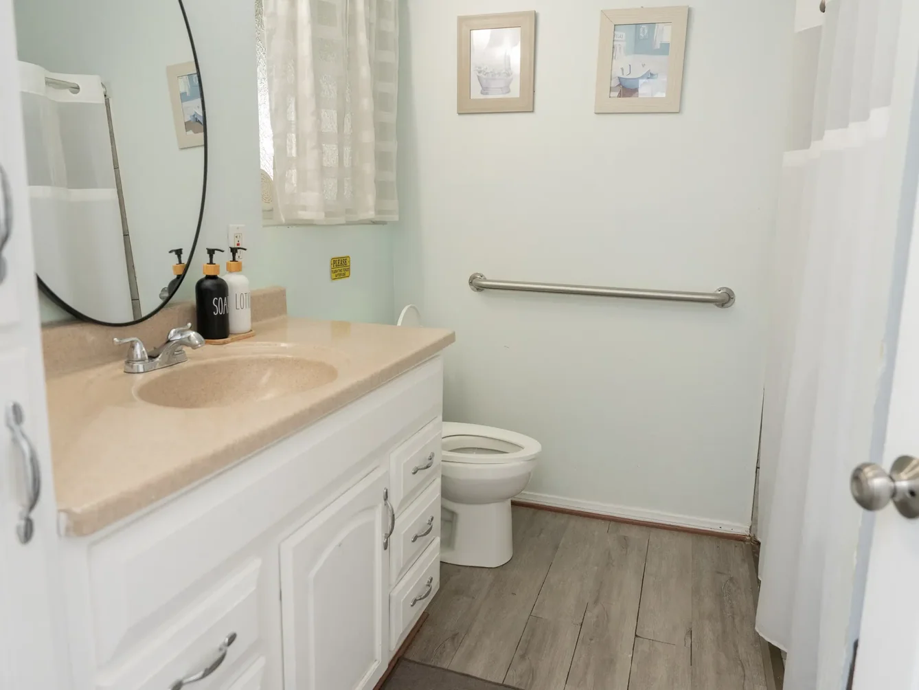 Clean, accessible bathroom featuring safety grab bar, white cabinetry with beige countertop, and modern fixtures.
