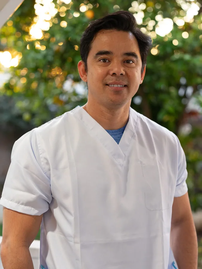 Friendly male caregiver in white medical scrubs smiling in outdoor setting